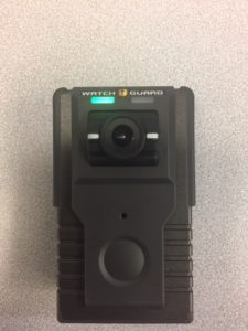 The body cam is a black rectangle with a round lens. It has a green light when active.